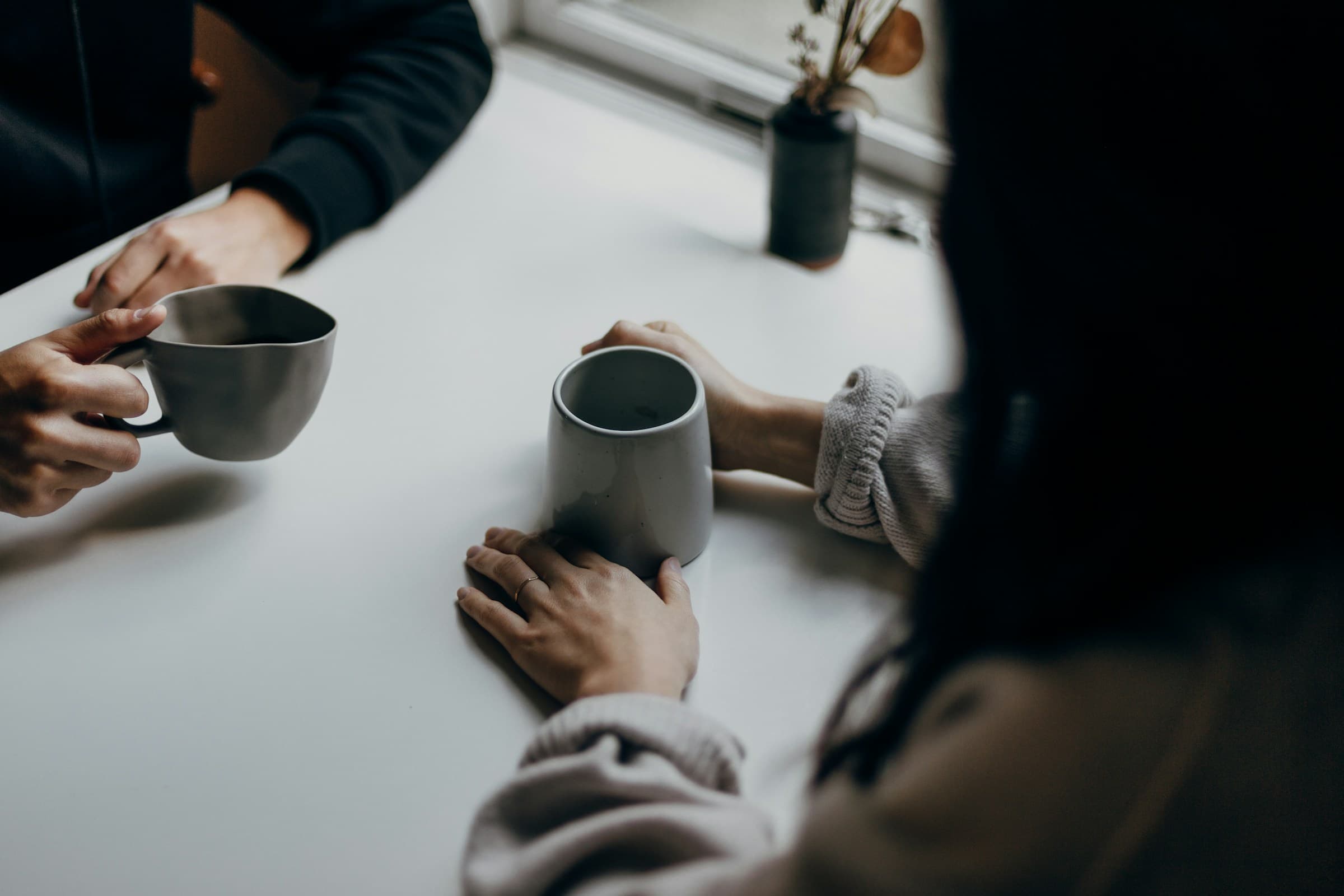 Two people sitting at a table together, each holding a mug