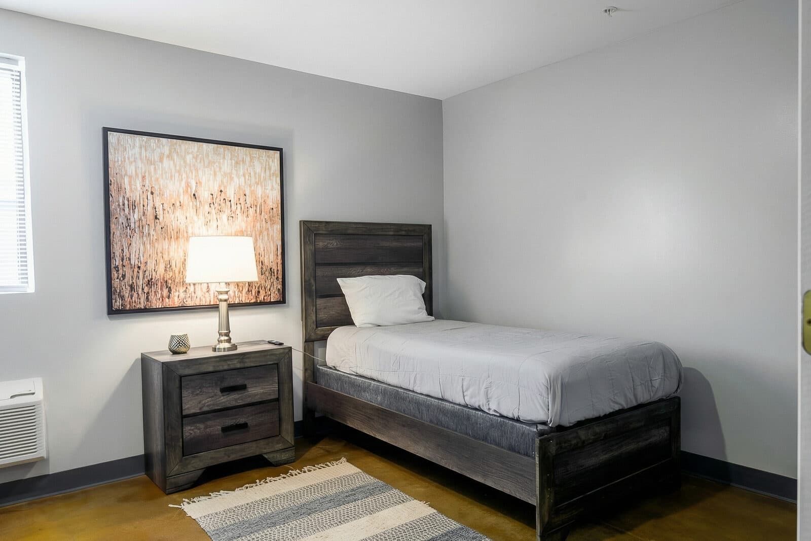 A single bed with white linens, a nightstand and lamp, and framed art in a private NSRC bedroom